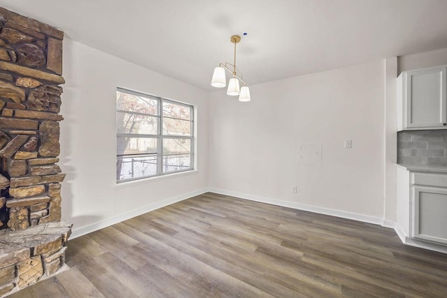 unfurnished living room with a stone fireplace, an inviting chandelier, and hardwood / wood-style floors