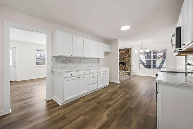 kitchen featuring a stone fireplace, decorative light fixtures, tasteful backsplash, and white cabinetry