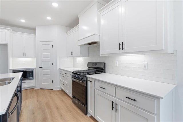 kitchen with white cabinets, light hardwood / wood-style floors, backsplash, black gas range oven, and stainless steel microwave