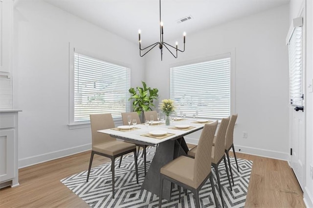 dining area with light wood-type flooring, a wealth of natural light, and an inviting chandelier