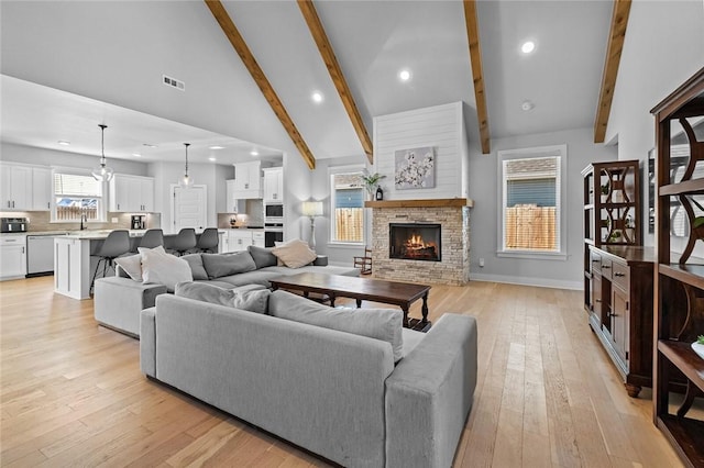 living room featuring light hardwood / wood-style flooring, a stone fireplace, high vaulted ceiling, beamed ceiling, and sink