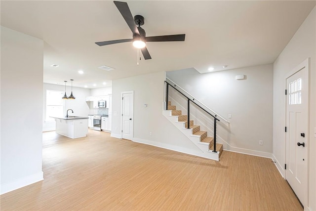 unfurnished living room featuring light wood-type flooring, a sink, baseboards, and stairs