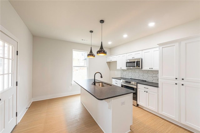 kitchen with tasteful backsplash, dark countertops, appliances with stainless steel finishes, a kitchen island with sink, and a sink