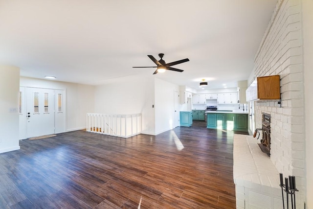 unfurnished living room with a sink, ceiling fan, baseboards, and dark wood-type flooring