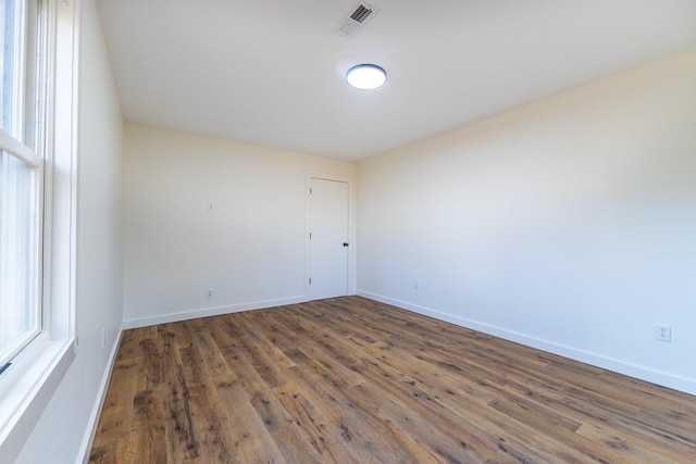 empty room with dark wood-style floors, a wealth of natural light, visible vents, and baseboards