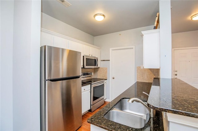 kitchen with appliances with stainless steel finishes, dark stone counters, decorative backsplash, white cabinets, and sink