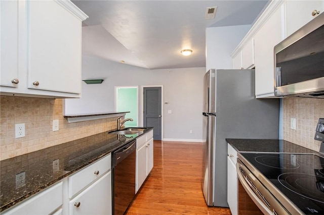 kitchen featuring stainless steel appliances, sink, white cabinets, light wood-type flooring, and dark stone counters