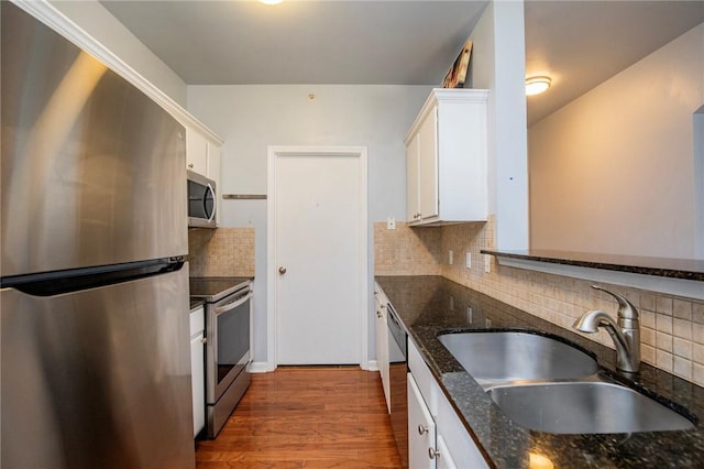 kitchen featuring stainless steel appliances, decorative backsplash, white cabinetry, dark stone counters, and sink