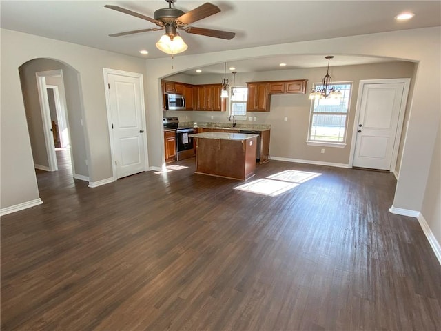 kitchen featuring dark wood-type flooring, hanging light fixtures, a center island, stainless steel appliances, and ceiling fan with notable chandelier