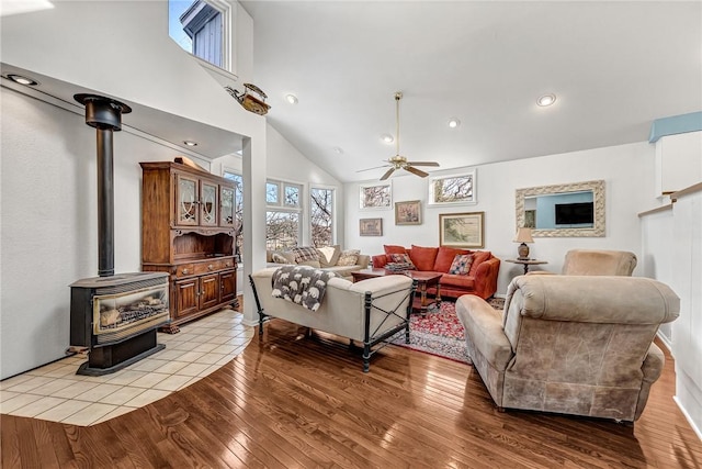 living room featuring ceiling fan, a wood stove, high vaulted ceiling, and light hardwood / wood-style floors