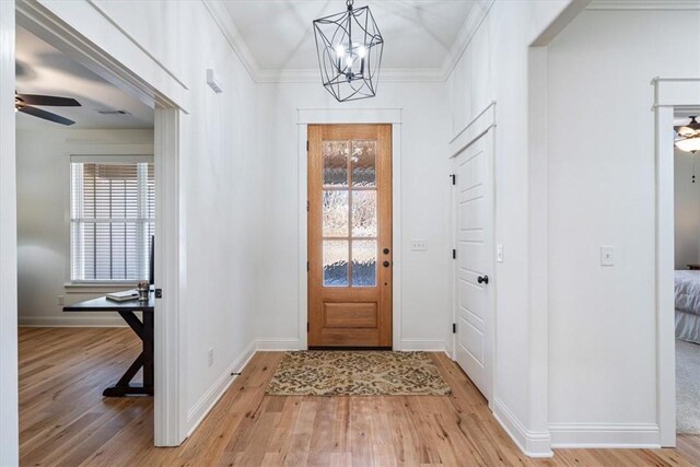 entrance foyer featuring ceiling fan with notable chandelier, ornamental molding, and light hardwood / wood-style flooring