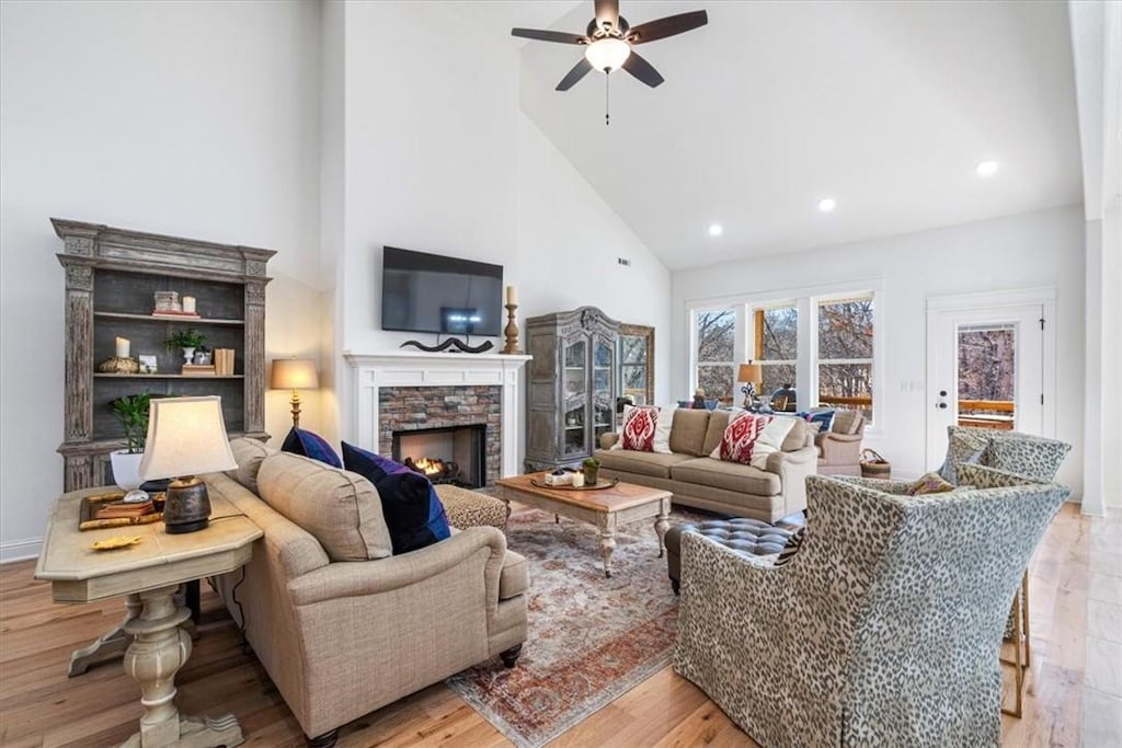 living room featuring ceiling fan, light hardwood / wood-style floors, a fireplace, and high vaulted ceiling