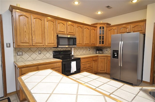 kitchen with light tile patterned floors, decorative backsplash, tile countertops, and stainless steel appliances