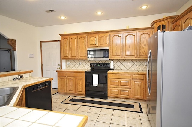 kitchen featuring decorative backsplash, light tile patterned floors, black appliances, and tile counters