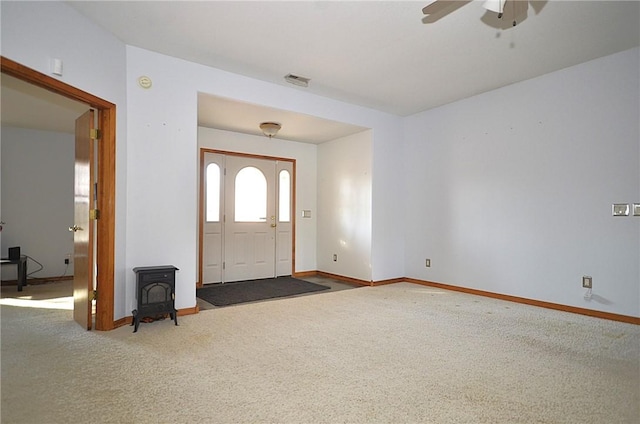 foyer entrance featuring ceiling fan, a wood stove, and carpet flooring