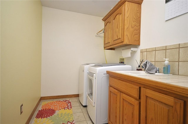 clothes washing area with washer and clothes dryer, sink, light tile patterned floors, and cabinets