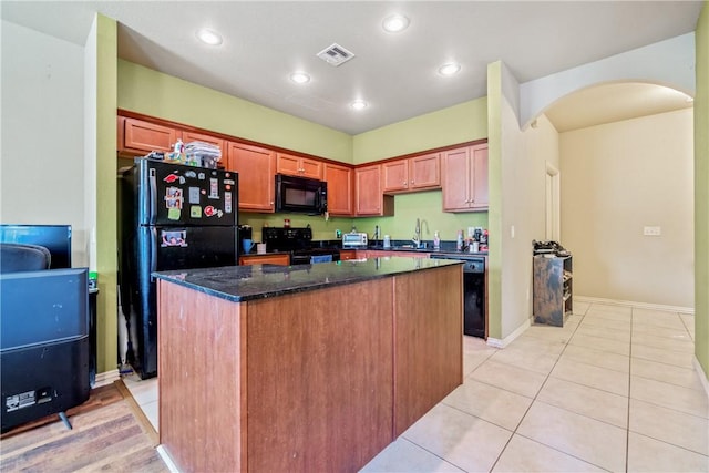 kitchen with dark stone countertops, a kitchen island, black appliances, sink, and light tile patterned floors