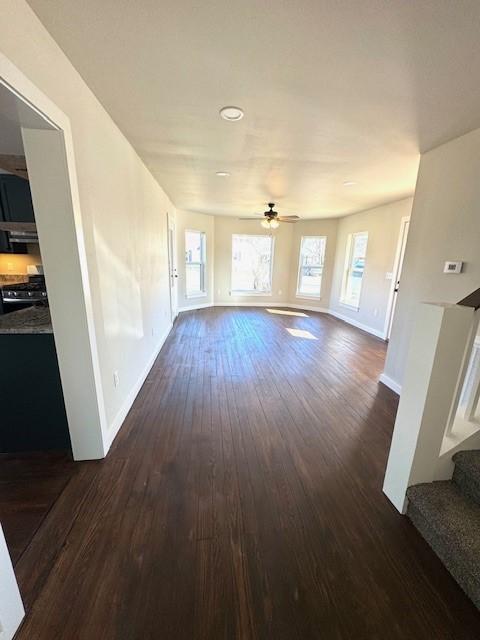 unfurnished living room featuring ceiling fan, stairs, dark wood-type flooring, and baseboards