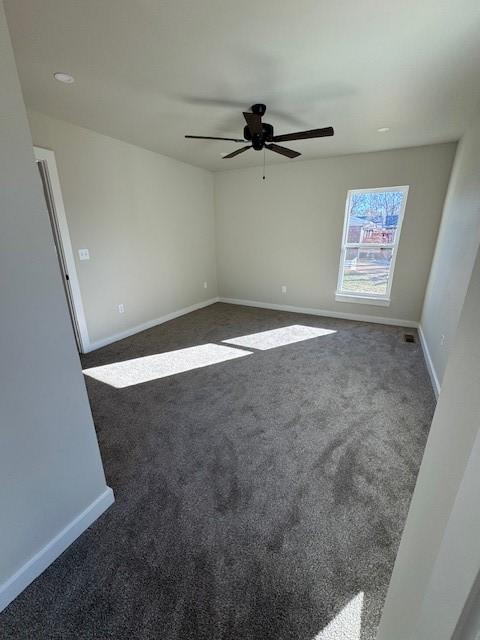 empty room featuring dark colored carpet, baseboards, and ceiling fan