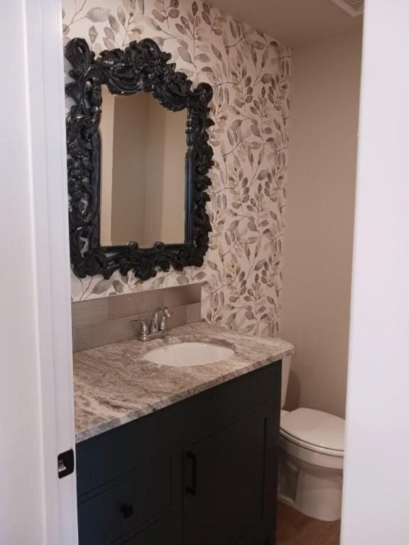 bathroom featuring toilet, wallpapered walls, and vanity