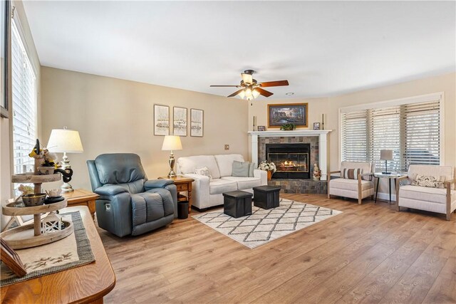 living room with ceiling fan, a tiled fireplace, and light hardwood / wood-style flooring