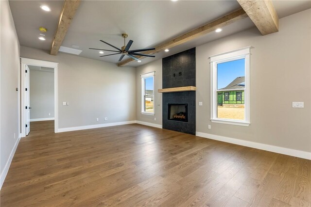 unfurnished living room featuring ceiling fan, wood-type flooring, beamed ceiling, and a fireplace