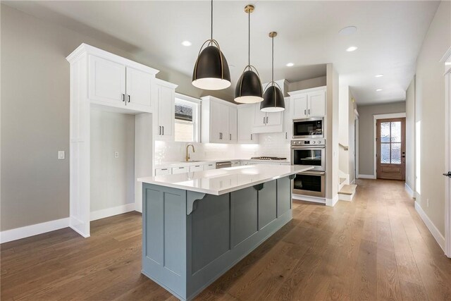 kitchen featuring white cabinets, a kitchen island, stainless steel appliances, backsplash, and hanging light fixtures