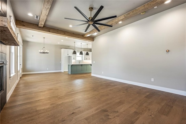 unfurnished living room featuring beam ceiling, ceiling fan with notable chandelier, and hardwood / wood-style floors