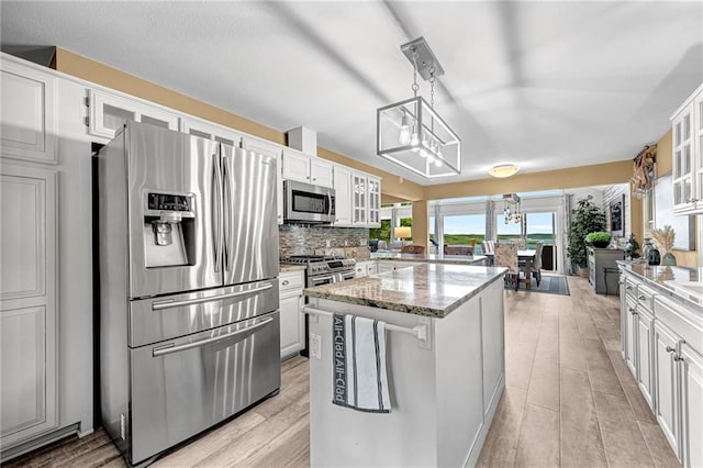 kitchen featuring appliances with stainless steel finishes, hanging light fixtures, light stone countertops, a kitchen island, and white cabinets