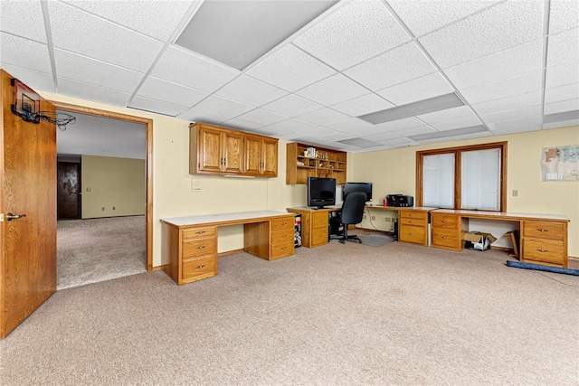 office space featuring a drop ceiling, built in desk, and light colored carpet