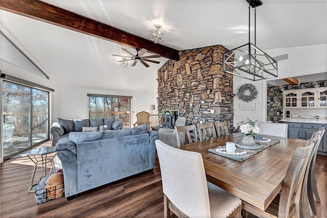 dining room with ceiling fan with notable chandelier, a stone fireplace, dark hardwood / wood-style floors, high vaulted ceiling, and beam ceiling