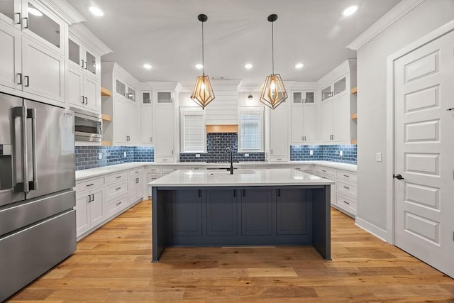 kitchen featuring white cabinetry, an island with sink, appliances with stainless steel finishes, decorative light fixtures, and sink