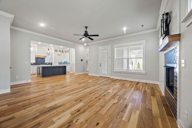 unfurnished living room featuring crown molding, light wood-type flooring, sink, and ceiling fan with notable chandelier