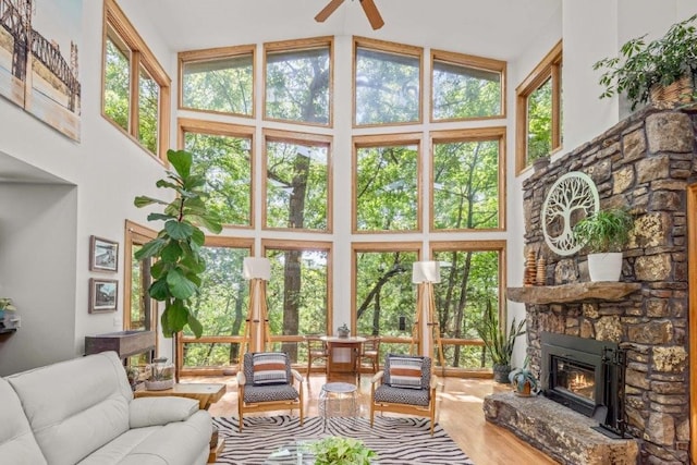 sunroom with ceiling fan, a stone fireplace, and lofted ceiling