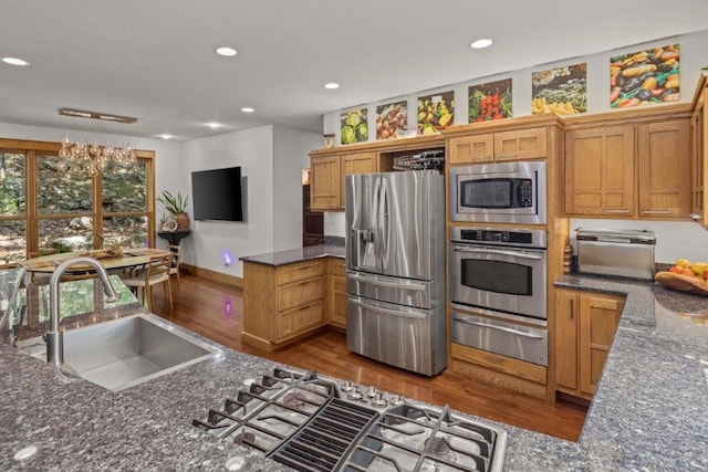 kitchen with dark stone countertops, pendant lighting, wood-type flooring, sink, and appliances with stainless steel finishes