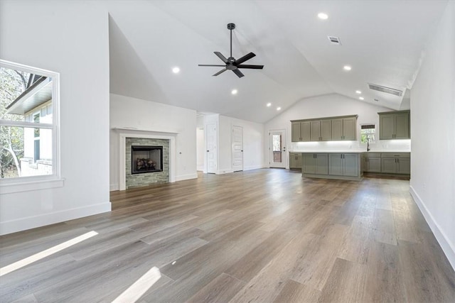 unfurnished living room with ceiling fan, hardwood / wood-style floors, a stone fireplace, and high vaulted ceiling