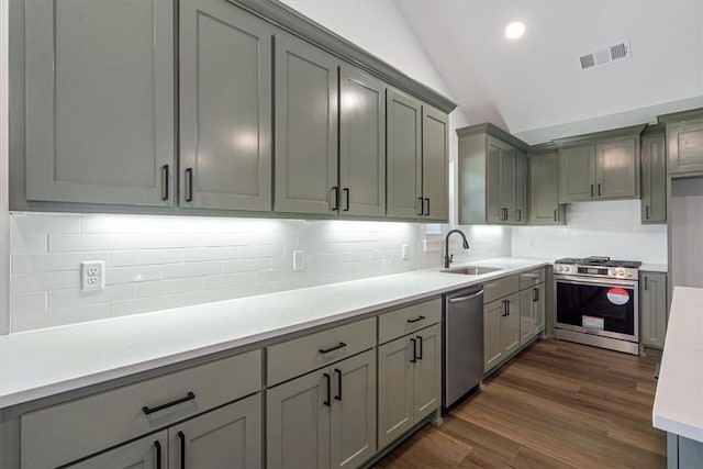 kitchen with stainless steel appliances, gray cabinetry, dark wood-type flooring, lofted ceiling, and sink