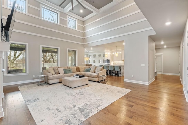 living room with hardwood / wood-style floors, a towering ceiling, coffered ceiling, ornamental molding, and a chandelier