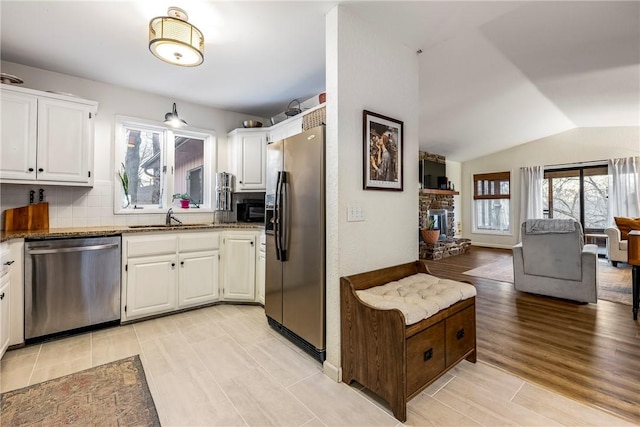 kitchen with appliances with stainless steel finishes, lofted ceiling, a fireplace, and white cabinets