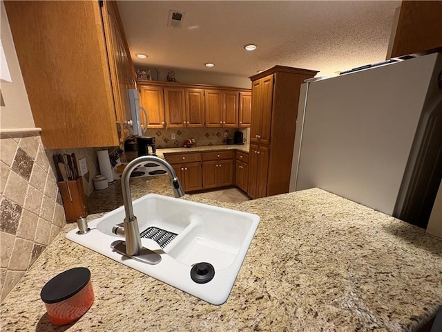 kitchen featuring kitchen peninsula, sink, light stone countertops, and stainless steel refrigerator