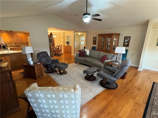 living room featuring light hardwood / wood-style floors, ceiling fan, a textured ceiling, vaulted ceiling, and sink