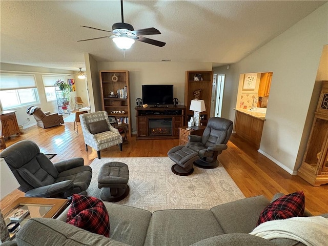 living room with ceiling fan, light wood-type flooring, a fireplace, and a textured ceiling