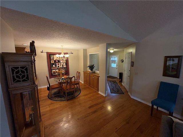 dining area featuring a textured ceiling, hardwood / wood-style floors, a fireplace, an inviting chandelier, and vaulted ceiling