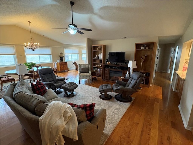 living room featuring ceiling fan with notable chandelier, hardwood / wood-style floors, a textured ceiling, and vaulted ceiling