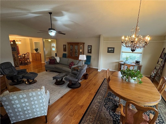 living room featuring lofted ceiling, wood-type flooring, ceiling fan with notable chandelier, and a textured ceiling