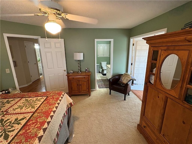 bedroom with ceiling fan, light colored carpet, a textured ceiling, and ensuite bath