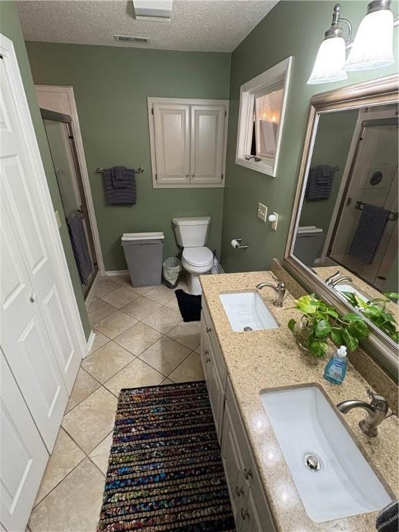 bathroom with toilet, vanity, tile patterned flooring, a textured ceiling, and an enclosed shower