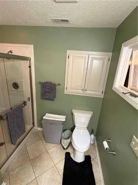 bathroom with toilet, tile patterned flooring, a textured ceiling, and a shower with door