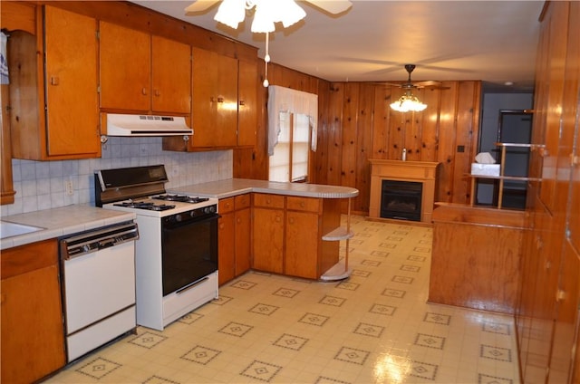 kitchen with under cabinet range hood, a peninsula, white appliances, a fireplace, and light floors