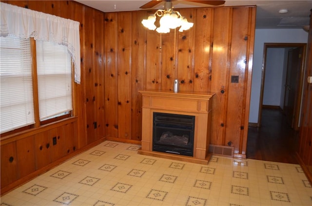 unfurnished living room with ceiling fan, a fireplace, visible vents, and wooden walls